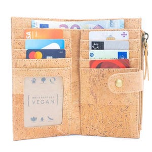 May include: Open brown cork wallet with multiple card slots and a zippered compartment. The wallet has a snap closure and a window for a photo or ID. The wallet is labeled "PETA Approved Vegan".