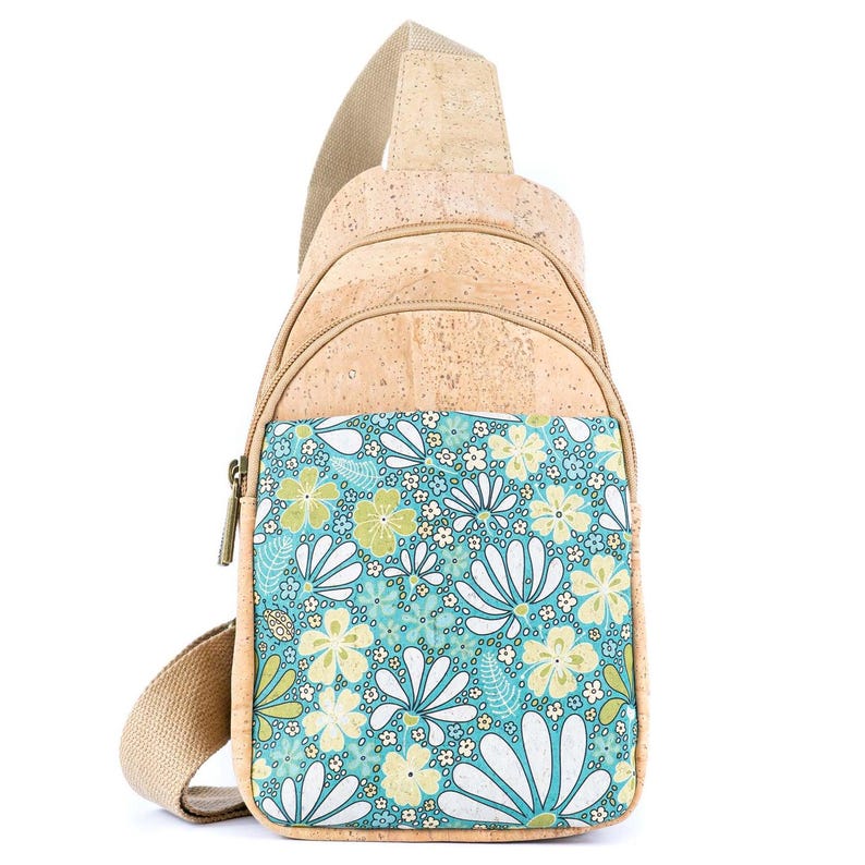 May include: A sling backpack crafted from light tan cork material featuring a front pocket with a vibrant teal, white, and pale yellow floral pattern. The bag includes a beige adjustable strap, a top zipper closure, and a secondary front zipper.