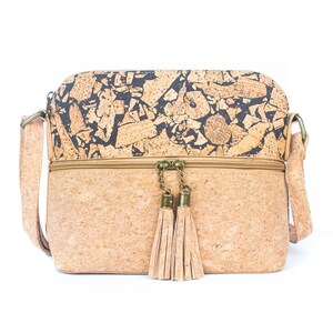 May include: A rectangular crossbody bag made of cork material. The top section features a black and brown pattern, while the bottom is a solid tan color. The bag has a zipper closure, a long adjustable strap, and two tan tassels hanging from the zipper.