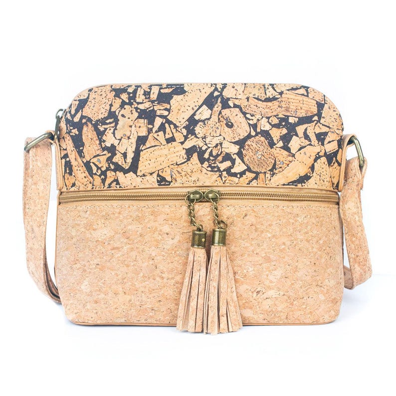 May include: A rectangular crossbody bag made of cork material. The top section features a black and brown pattern, while the bottom is a solid tan color. The bag has a zipper closure, a long adjustable strap, and two tan tassels hanging from the zipper.