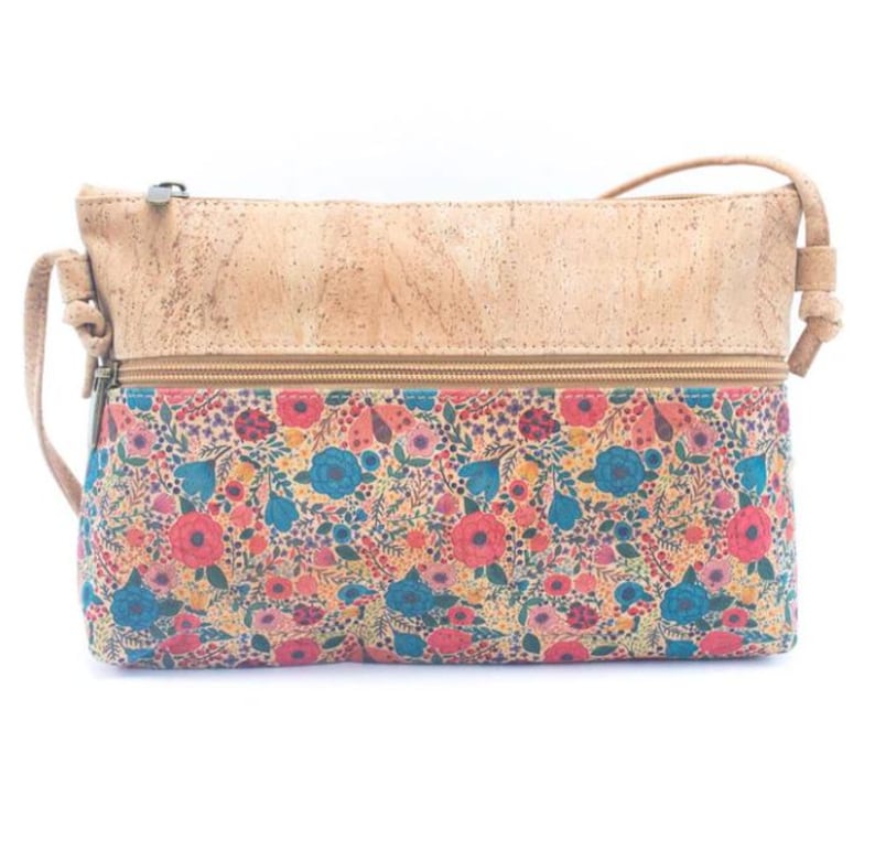 May include: A crossbody bag with a floral pattern and a cork top. The bag features a colorful floral print with red, blue, and yellow flowers. The top of the bag is made of light brown cork material. The bag has a zipper closure and a long strap.