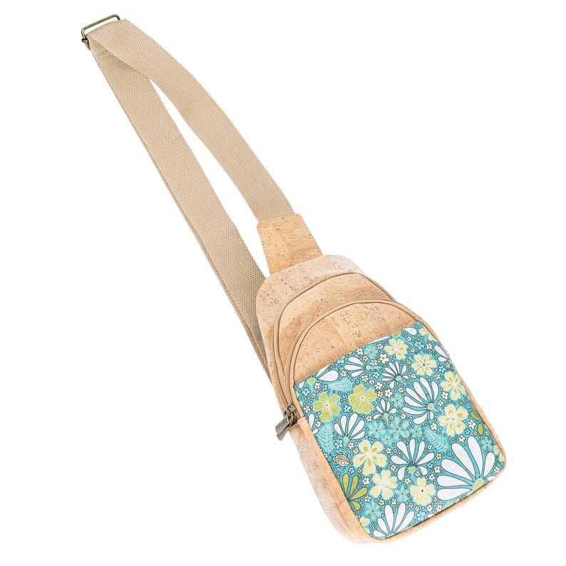 May include: A sling bag crafted from light brown cork material featuring a beige adjustable strap and a front pocket decorated with a vibrant floral pattern in shades of teal, light green, and white, secured with a metal zipper closure.