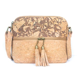 May include: A crossbody bag made of cork material. The bag features a rectangular shape with a zipper closure and a long adjustable strap. The top section has a mosaic design, and the bottom section is a solid color. Two tassels hang from the zipper.