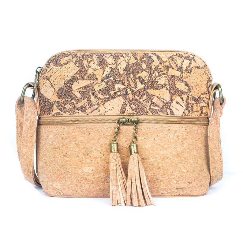 May include: A crossbody bag made of cork material. The bag features a rectangular shape with a zipper closure and a long adjustable strap. The top section has a mosaic design, and the bottom section is a solid color. Two tassels hang from the zipper.