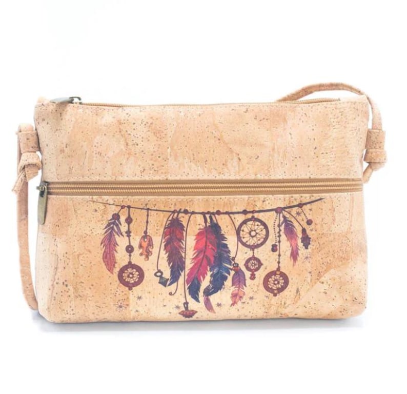 May include: A light brown cork crossbody bag with a zipper closure and adjustable strap. The bag features a colorful dreamcatcher design with feathers in shades of red, purple, and blue. The bag is rectangular in shape.