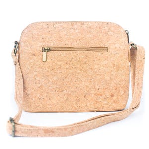 May include: A light brown cork crossbody bag with a zipper closure and adjustable strap. The bag has a rectangular shape with rounded corners and a textured surface. The strap and zipper are a matching light brown color.