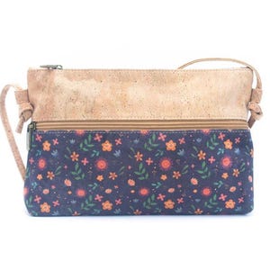 May include: A rectangular crossbody bag with a natural cork top and a navy blue floral patterned bottom. The bag features a zipper closure and a thin shoulder strap. The floral pattern includes orange and pink flowers with green leaves.