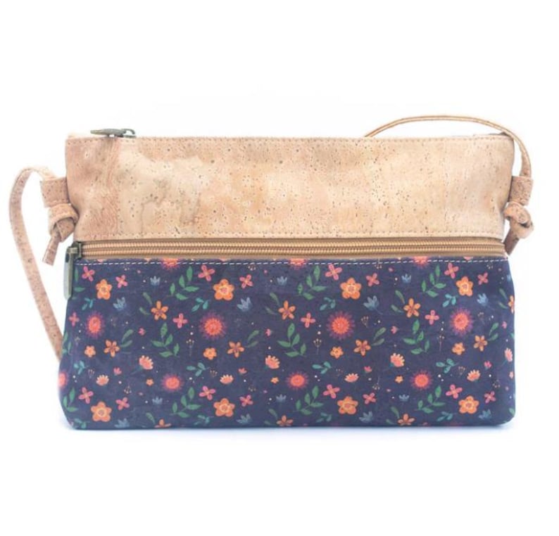 May include: A rectangular crossbody bag with a natural cork top and a navy blue floral patterned bottom. The bag features a zipper closure and a thin shoulder strap. The floral pattern includes orange and pink flowers with green leaves.