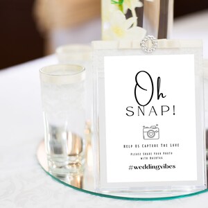 Peut inclure: Une pancarte blanche avec du texte noir qui dit "Oh SNAP!" avec une icône d'appareil photo et le texte "Aidez-nous à capturer l'amour. Veuillez partager votre photo avec le hashtag #weddingvibes".