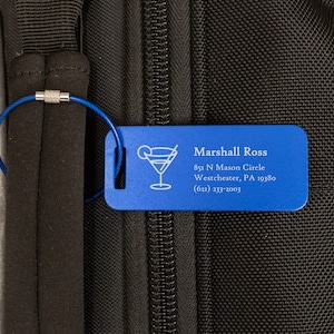 May include: Blue luggage tag with a silver cable attached. The tag has a cocktail glass icon and the text "Marshall Ross", "851 N Mason Circle", "Westchester, PA 19380", and "(621) 233-2003".