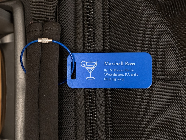May include: Blue luggage tag with a silver cable attached. The tag has a cocktail glass icon and the text "Marshall Ross", "851 N Mason Circle", "Westchester, PA 19380", and "(621) 233-2003".