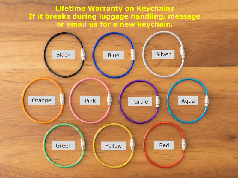 May include: Twelve different colored keychains made of metal wire. The keychains are arranged in a circle on a wooden surface. The colors are black, blue, silver, orange, pink, purple, aqua, green, yellow, and red.
