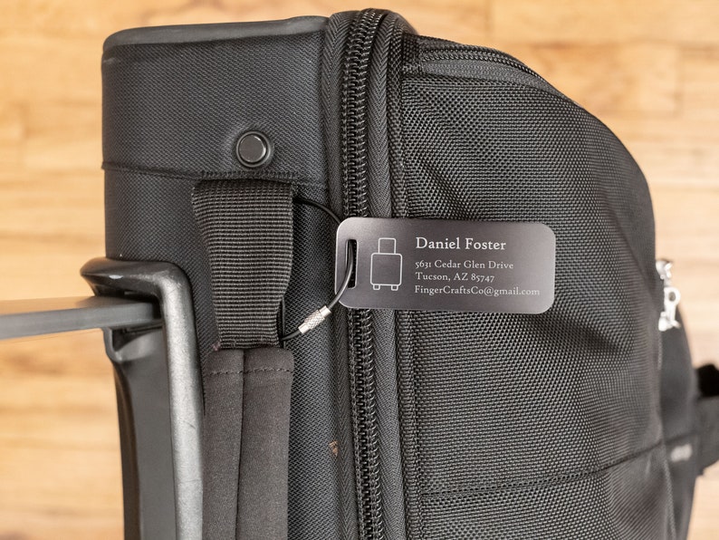 May include: Black luggage tag with a silver luggage icon and the text "Daniel Foster", "5615 Cedar Glen Drive", "Tucson, AZ 85747", and "FingerCraftsCo@gmail.com".