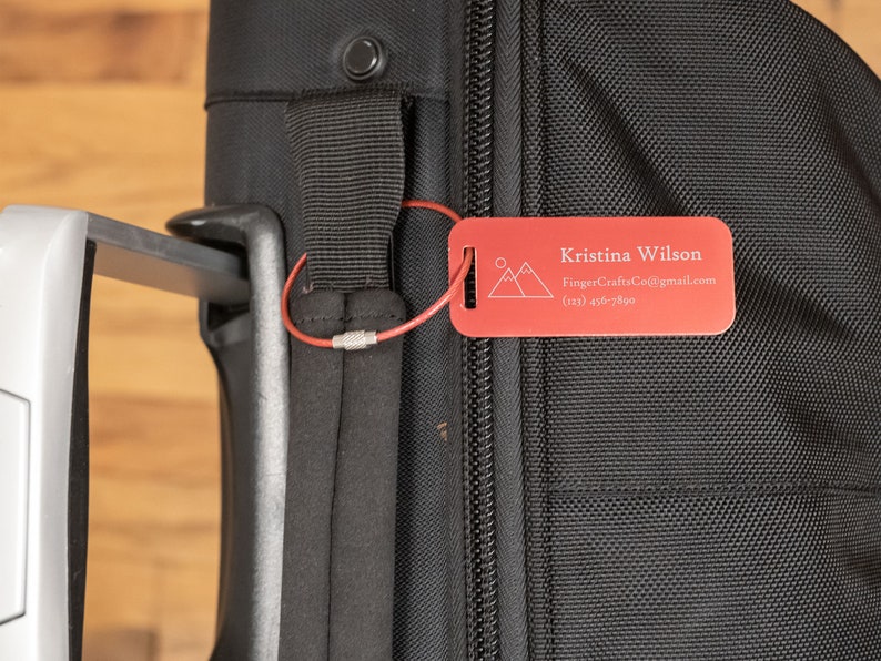 May include: Red luggage tag with a mountain design and the text "Kristina Wilson", "FingerCraftsCo@gmail.com", and "(123) 456-7890".