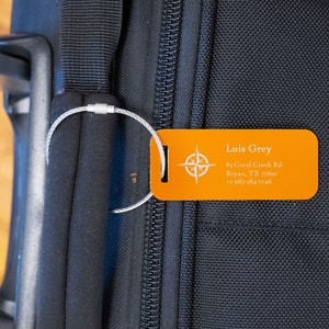 May include: Orange luggage tag with a compass design and the text "Luis Grey", "81 Coral Creek Rd", "Bryan, TX 77801", and "+1-983-284-1746".