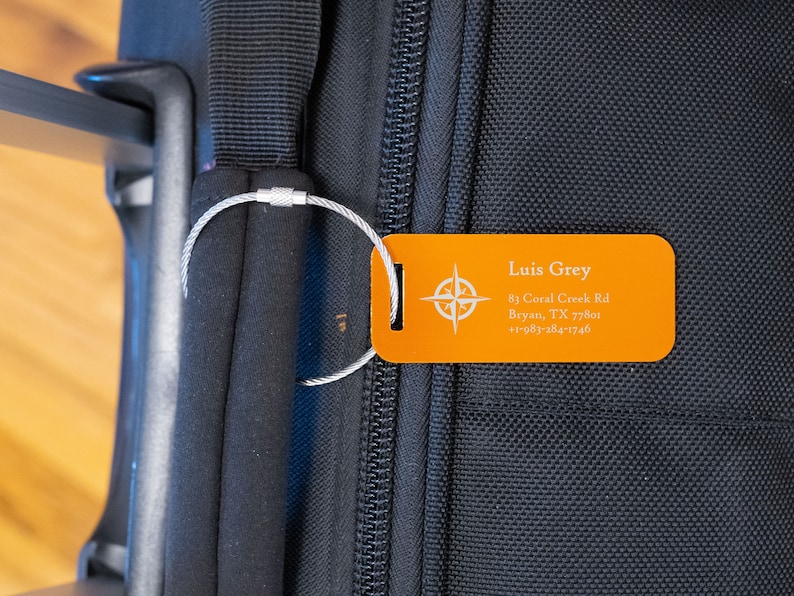 May include: Orange luggage tag with a compass design and the text "Luis Grey", "81 Coral Creek Rd", "Bryan, TX 77801", and "+1-983-284-1746".