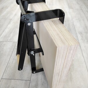 K&ouml;nnte beinhalten: Ein schwarzer Metallst&auml;nder mit einer Holzrolle und einem Stapel Sperrholzplatten. Der St&auml;nder ist so konzipiert, dass er die Sperrholzplatten h&auml;lt und transportiert.