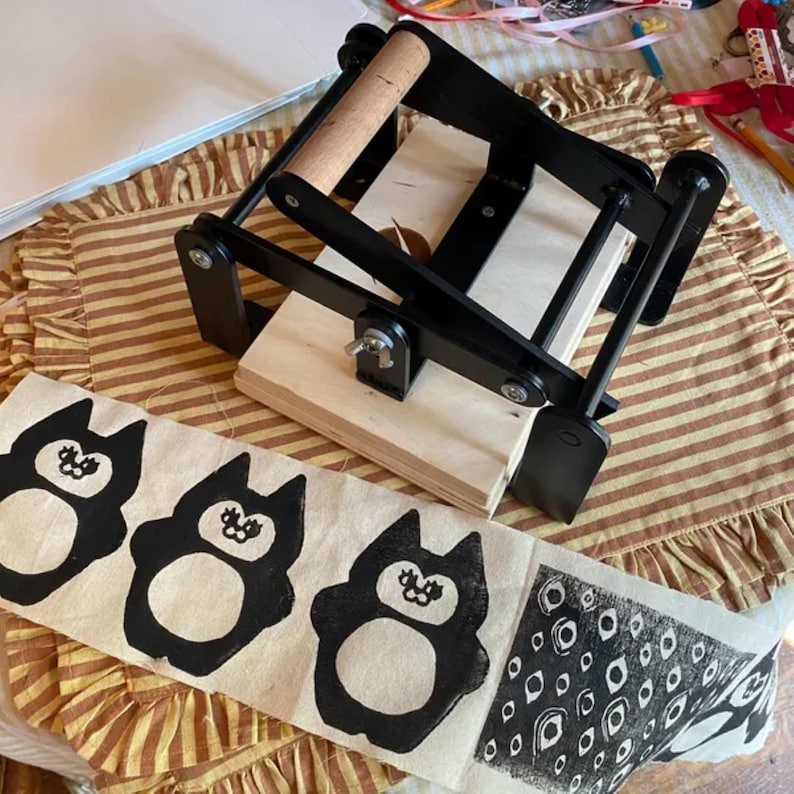 May include: A black and wooden printing press with a fabric print of black cartoon animals and a geometric pattern. The fabric is on a striped surface.