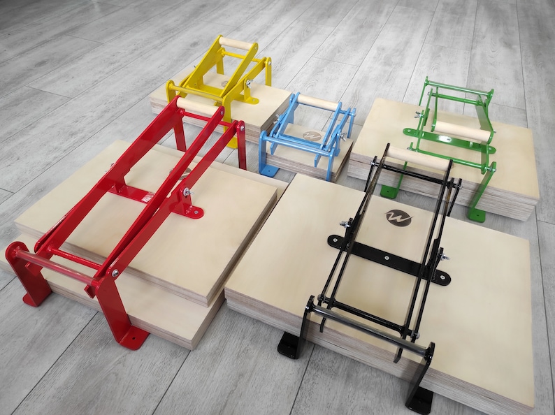 May include: Five different colored printing presses with wooden handles. The presses are made of metal and are stacked on top of wooden boards. The presses are used for printing on fabric, paper, and other materials.