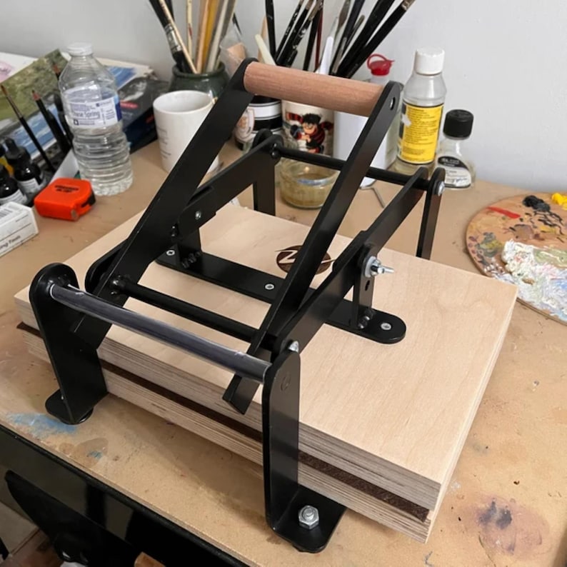 May include: A black metal book press with a wooden handle. The press is made of metal and has a wooden handle. The press is used to press books.