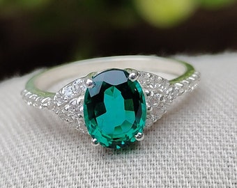 May include: A silver ring featuring a large oval emerald green gemstone, surrounded by smaller clear gemstones.