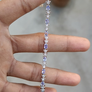 Può includere: Un braccialetto d'argento con una fila di pietre ovali blu e pietre trasparenti più piccole incastonate in un motivo triangolare.