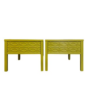 May include: A pair of yellow end tables with a geometric pattern on the top. The tables have four legs and are made of wood.