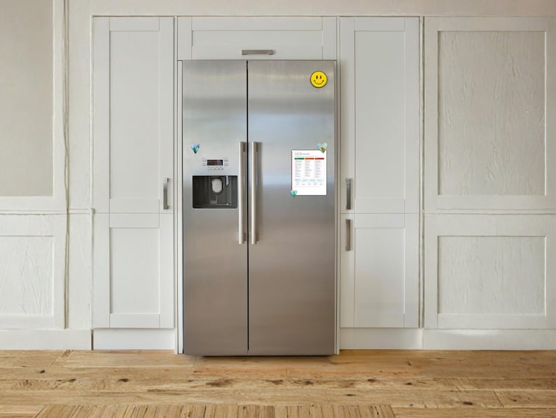 May include: A stainless steel side-by-side refrigerator with a water and ice dispenser on the left door. A yellow smiley face magnet is at the top, and a rectangular white chart with text and coloured rows is attached to the right door with magnets.
