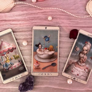 May include: Three rectangular tarot cards featuring whimsical illustrations. The left card shows a carousel with a figure, the center card depicts a figure in a bubble bath with a gingerbread man, and the right card shows a figure in a cake dress.