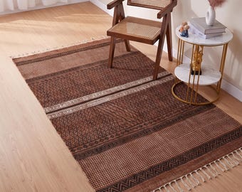 May include: A rectangular area rug featuring a deep brown base with intricate black geometric patterns, including diamond shapes, horizontal stripes, and dotted sections. The rug is finished with off-white fringe tassels along the shorter edges.