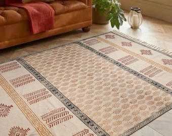 May include: A rectangular area rug featuring a cream-colored base with repeating brown geometric patterns, including diamond shapes, chevron stripes, and border motifs. The rug is finished with short, knotted fringe along the edges.
