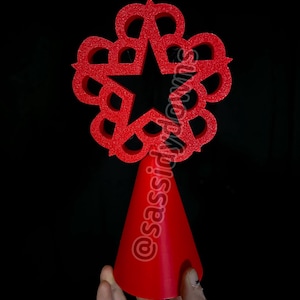 May include: A red decorative object with a star-shaped center and a floral-like design, atop a red cone. The object has a glittery texture. The background is black. The text "@sassidydowns" is visible.