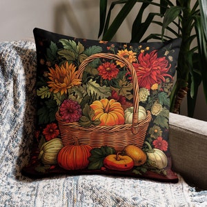 Puede incluir: Un coj&iacute;n cuadrado con fondo oscuro que muestra una cesta de mimbre llena de calabazas naranjas, girasoles amarillos y dalias de color rojo intenso. El dise&ntilde;o incluye follaje verde y peque&ntilde;as calabazas dispuestas alrededor de la cesta.