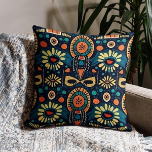 May include: A decorative throw pillow with a blue background and a colorful geometric pattern featuring yellow, orange, and green accents. The pattern includes stylized flowers and circles.