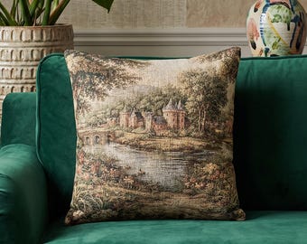 May include: A square scatter cushion featuring a woven tapestry design of a castle landscape with a stone bridge, a river, and lush trees. The cushion is placed on a solid dark green velvet sofa, showcasing detailed earth-toned threads and textures.