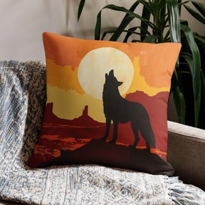 May include: A throw pillow with a sunset scene featuring a coyote howling at the moon. The coyote is a silhouette against the orange and red sky. The moon is a large, white circle in the sky.