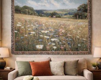 Puede incluir: Un tapiz de pared rectangular tejido que muestra un paisaje de pradera con flores blancas, azules y rosas bajo un cielo nublado. El tapiz tiene un borde con flecos y está suspendido de una barra horizontal de metal de latón.