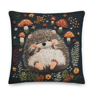 May include: Square throw pillow with an embroidered design featuring a smiling hedgehog surrounded by mushrooms, flowers, and foliage. The color palette includes shades of brown, orange, green, and white on a dark blue background.