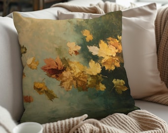May include: A decorative throw pillow featuring an artistic rendering of falling autumn leaves. The pillow displays a palette of warm colors, including shades of yellow, orange, and brown, set against a teal and green background. The pillow is square and appears to be made of soft fabric.