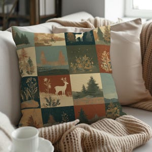 May include: Square throw pillow with a patchwork design featuring forest scenes and deer silhouettes in shades of green, brown, and beige. The pillow is placed on a white sofa with a neutral-colored blanket.