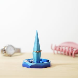 May include: A blue and white ring holder with a pointed top and a ring on the top. The holder is on a wooden surface.