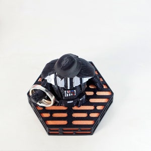 May include: A black Darth Vader figurine holding two silver rings on a hexagonal orange and black platform.