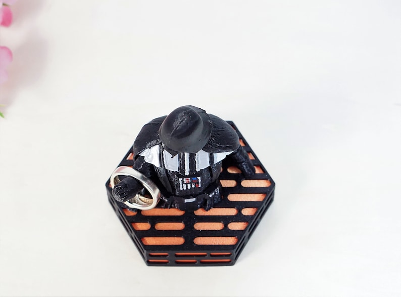 May include: A black Darth Vader figurine holding two silver rings on a hexagonal orange and black platform.