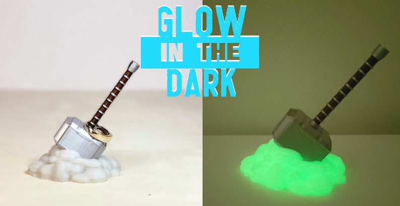 May include: A silver and brown Mjolnir hammer prop glows green in the dark. The hammer is on a white cloud-like base. The text "GLOW IN THE DARK" is in blue letters on a white background.
