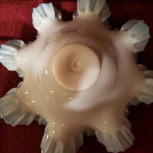 May include: A white milk glass bowl with a scalloped edge and a blue iridescent finish. The bowl has a round base and is designed to hold small items.