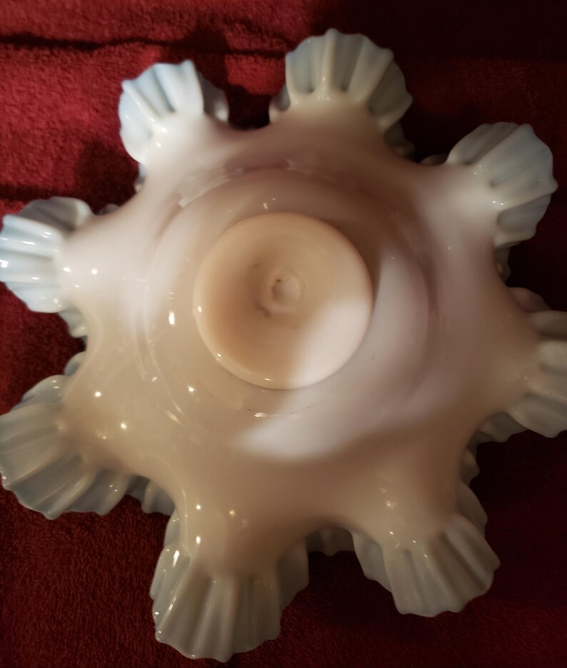May include: A white milk glass bowl with a scalloped edge and a blue iridescent finish. The bowl has a round base and is designed to hold small items.