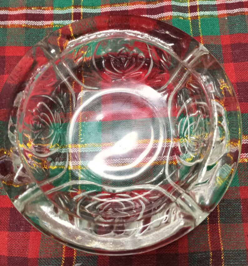 May include: A clear glass ashtray with a decorative floral design. The ashtray has four sections and is round.
