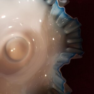 May include: A white milk glass bowl with a blue ruffled edge. The bowl is a vintage style and has a delicate design.