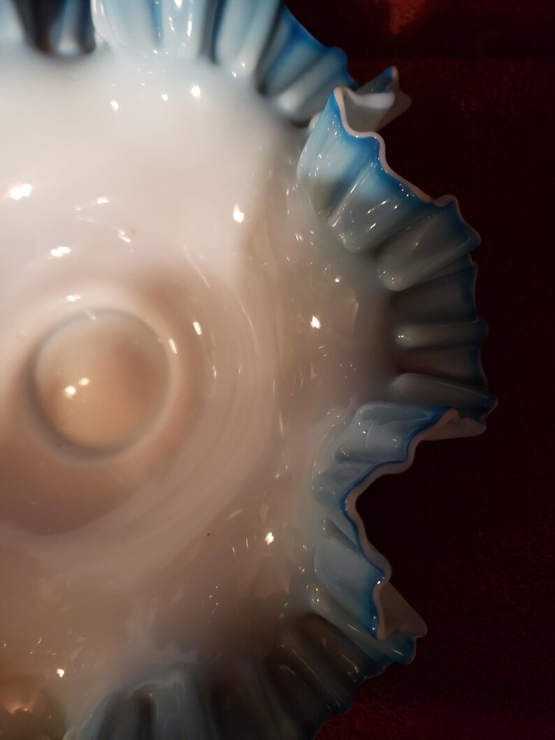 May include: A white milk glass bowl with a blue ruffled edge. The bowl is a vintage style and has a delicate design.
