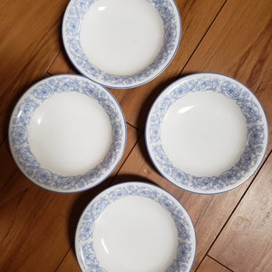 Può includere: Quattro ciotole in ceramica bianca con un motivo floreale blu intorno al bordo. Le ciotole sono su una superficie di legno.